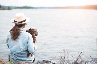 Mutlu Genç Asyalı kadın köpeğini rezervuar yanında oturuyor. Açık zevk Güzellik genç kız yaz tatili doğa manzaralı ve nehir içinde pets ile seyahat. Özgürlük ve dostluk kavramı.