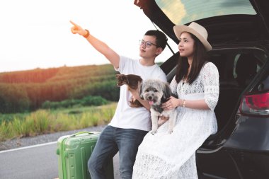 Hayattan zevk mutlu ve Genç Asyalı Çift Evcil ile seyahat. Kırsal köpeklerle oynamak araba bagajı oturan çift yolcuları. Genç aile yaşam tarzı seyahat macera ve açık hava tatil.