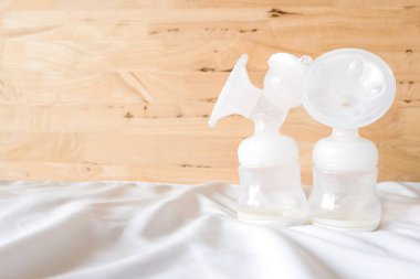 Taze anne anne sütü ile otomatik göğüs pompası bebek beyaz çarşaf ve yatak odasında ahşap arka plan için şişe. Göğüs pompası ve mağaza buzdolabı yardım Anne sütü daha taze kal.