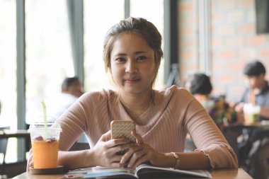 Portre genç güzel Asyalı kadın gülümseme ve okuma Dergisi kitap ve içki portakal suyu smoothie Cafe, smartphone tutan el ahşap masa üzerinde. Dinlenme, Relax ve yaşam tarzı.