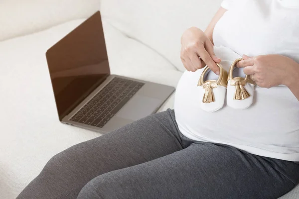 Feliz Mulher Grávida Mão Segurando Sapatos Bebê Enquanto Sentado Sofá — Fotografia de Stock