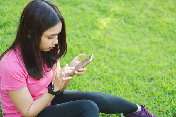 Молодая фитнес-женщина с помощью смартфона для проверки спортивного приложения отслеживания прогресса и отдыха в парке после тренировки и бегать. Бегунья в длину одевается сидя и пользуясь телефоном на открытом воздухе
.