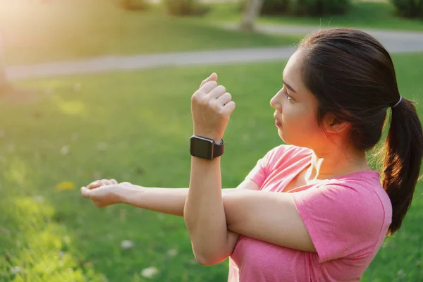 Young asian fitness woman stretching arms, tricep and shoulders before and after exercise in park at morning. Healthy female in smartwatch tracker warming up outdoor. Healthy and lifestyle concept.