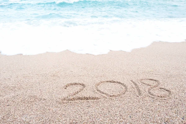 Happy new year 2018 concept. Number 2018 written on sandy beach with blue sea waves and foam. Holiday, vacation and new year celebration on tropical summer beach.