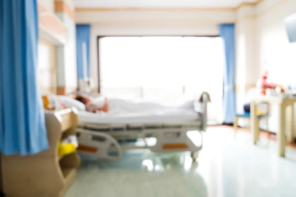 Blurred background of patient lying on bed in hospital room with nature light from window. Blurry image of recovery room with bed and comfortable medical equipped for patient for background.