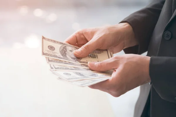 Happy and successful businessman holding US dollar money bills in hand. Close up  hand showing and counting cash in concept of investment, success, freedom, financial prospects, career advancement.