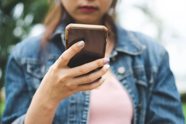 Genç kız Smartphone açık kullanarak kapatın. Kot ceket yazmak ve mesaj okuma giyen hipster kadın cep telefonu video içeriği izliyor. Sosyal ve teknoloji kavramı.