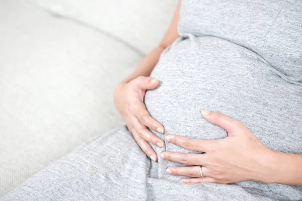 Szczęśliwy Piękne Kobiety Ciąży Siedząc Szary Kanapie Domu Ręką Dotykając — Zdjęcie stockowe