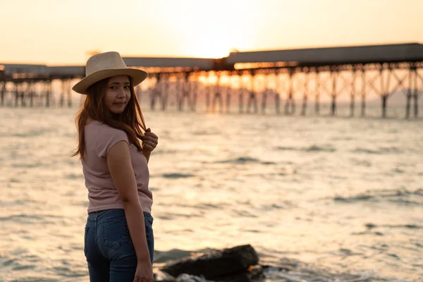 一个美丽的亚洲妇女的肖像在沙滩上站在户外日落的稻草帽 在海边和木桥享受自然夏日傍晚的少女 假日假期 阳光照耀海上 — 图库照片