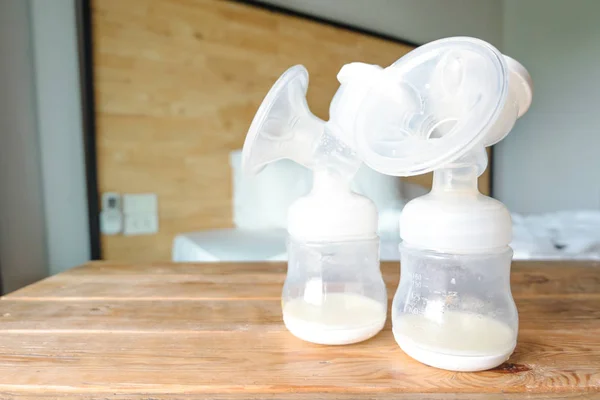 Bottles of automatic breast pumping with fresh mother breast milk for baby on wooden table and wooden background in bedroom. Breast pump and store in refrigerator help breast milk stay fresh longer.