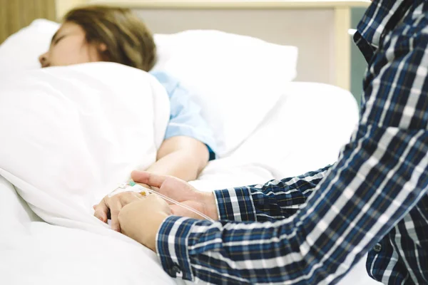 Kadın hasta el güven verici ve teşvik karısı için hastanede yatağında intravenöz enjeksiyonla serum fizyolojik çözüm alma tutan adam el. Tıbbi tedavi, sağlık, Aile ve sevgi kavramı.