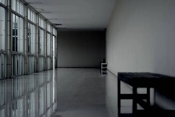 Dark empty walkway in building hall perspective with long white wall on left and long windows with light on left, minimalist black and blurred bench, Horror Halloween background used.