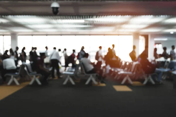 Blurred defocused image of travelers queue in terminal departure check-in point at international airport. Many people sitting on chair in gate waiting zone, waiting for flight to destination.