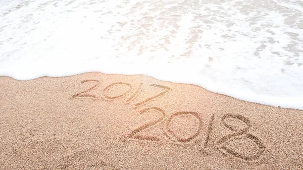 Happy new year 2018 is coming and replace 2017 concept. Number 2018 written on sandy beach with blue sea waves and foam. Holiday, vacation and new year celebration on tropical summer beach.