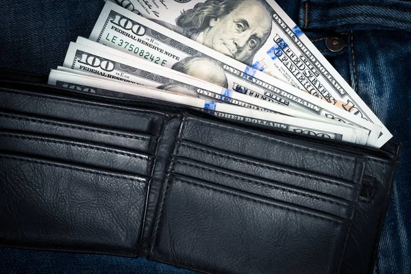 Siyah deri cüzdan boş kredi kartı yuvaları para kopya alanı mavi jean zemin üzerine yerleştirilir. Yüz dolar faturaları siyah çanta içinde yığını.