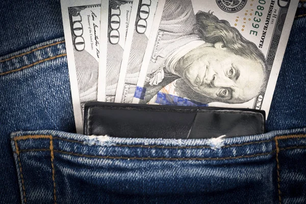Close up money and wallet in pocket of blue jean. One hundred dollar bills in back of jean pocket.