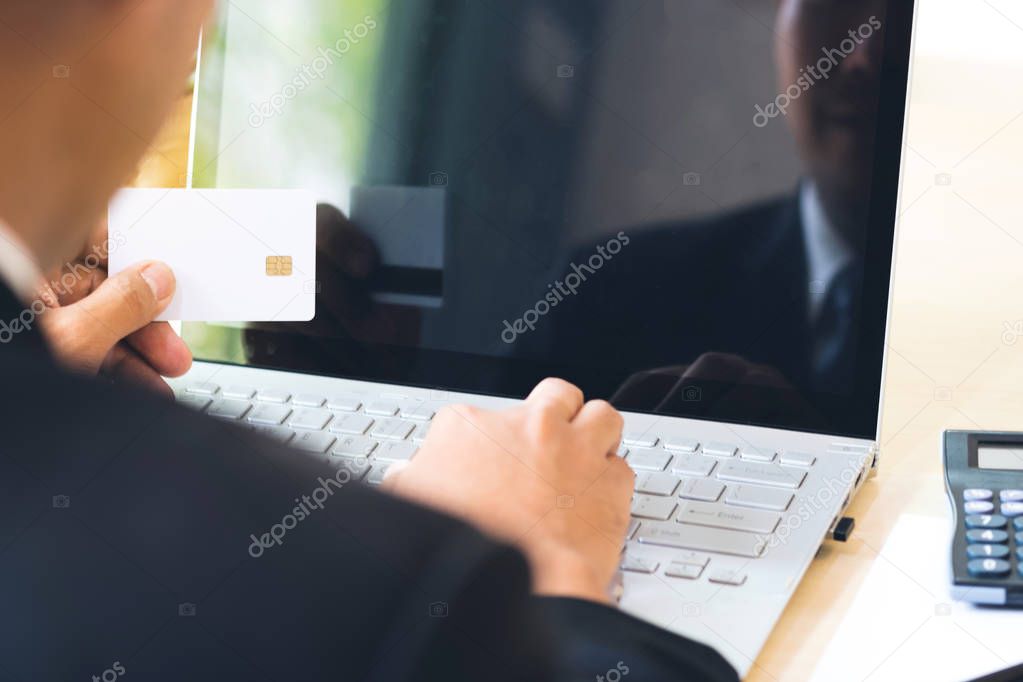 Businessman hand holding credit card and using laptop on desk with document and calculator. Man hand use card for online shopping and online payment cashless society concept.