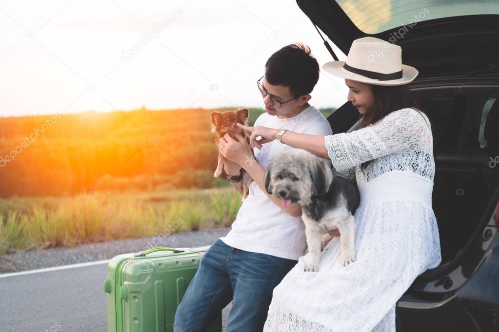Happy and young asian couple enjoying life travel lifestyle with pets. Couple travelers sitting in hatchback car playing with dogs while parking. Young family travel adventure and outdoor vacation.