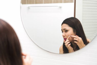 Genç Asyalı kadın banyoda yüzünde sivilce ile aynaya bakıyor. Sivilce yüzünü çıkarmak güzel kız onun sivilce sıkma. Cilt Bakımı. Akne cilt sorunu üzerinde spot acil.