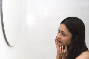 Genç Asyalı kadın banyoda yüzünde sivilce ile aynaya bakıyor. Sivilce yüzünü çıkarmak güzel kız onun sivilce sıkma. Cilt Bakımı. Akne cilt sorunu üzerinde spot acil.