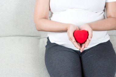 Genç ve aşk kırmızı kalp el karnının önünde tutan mutlu hamile kadın. Annenin kalp sağlık, umut ve bekliyor, insanlar, ebeveynlik, Aile ve sağlık kavramı.