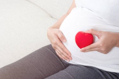 Genç ve aşk kırmızı kalp el karnının önünde tutan mutlu hamile kadın. Annenin kalp sağlık, umut ve bekliyor, insanlar, ebeveynlik, Aile ve sağlık kavramı.