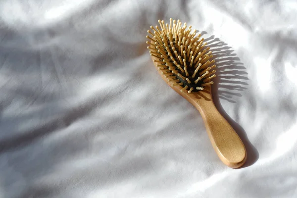 Hair fall, Hair loss problem. Wooden brown comb with hair loss on white bed cover. Woman healthy and beauty concept.