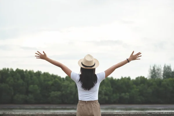 快乐的时髦女人穿着白衬衫和帽子 在傍晚的日落时分 在河边保持户外开放的手 愉快的年轻女孩旅行者在湖享受时间 生活方式旅行 放松和自由概念 — 图库照片
