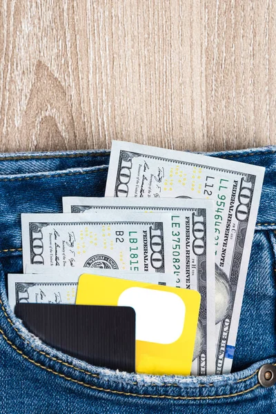 Money, Debit card and Credit card are in pocket of blue jean on wooden background with copy space. One hundred dollar bills and cards in back of jean pocket in concept of business and finance.