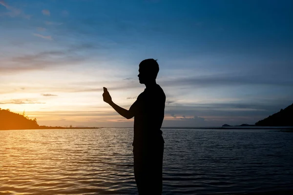 穏やかな青い海と熱帯のビーチで一人で立って 美しい夕暮れ夕暮れ時スマート フォンを保持している人のシルエット 孤独な男のコンセプト — ストック写真