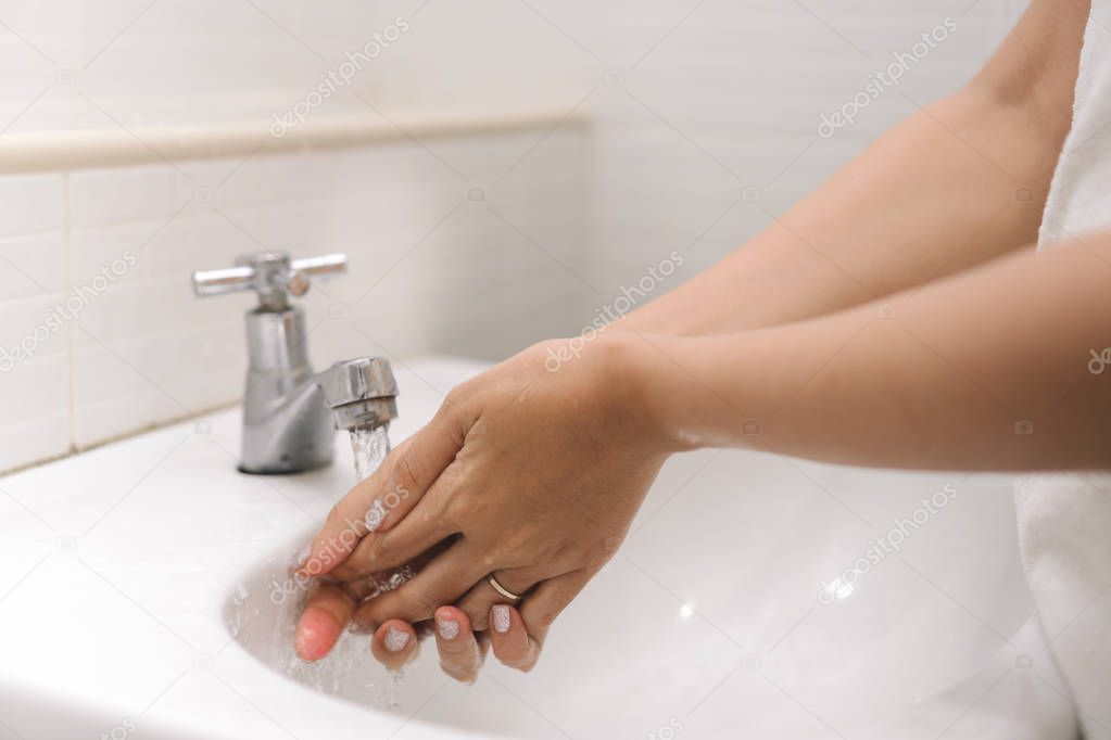 Close up woman is washing her hand under running water in bathroom. Hygiene. Cleaning hands at washbasin.