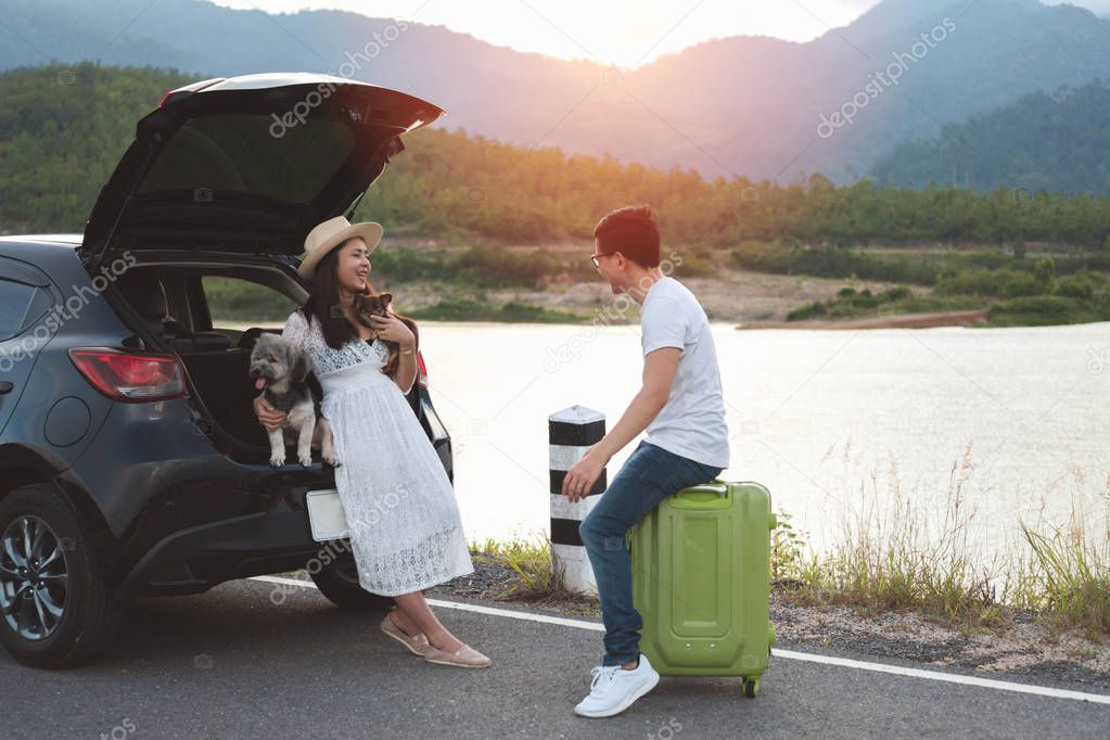 Happy and young asian couple enjoying life travel with pets. Couple travelers sitting in car trunk playing with dogs at countryside. Young family lifestyle travel adventure and outdoor vacation.