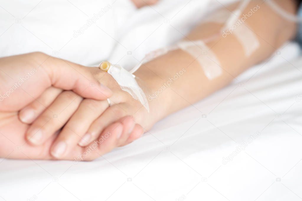 Selective focus on man hand holding woman patient's hand receiving saline solution by intravenous injection on bed in hospital for reassuring and encouragement his wife. Medical treatment, healthcare.