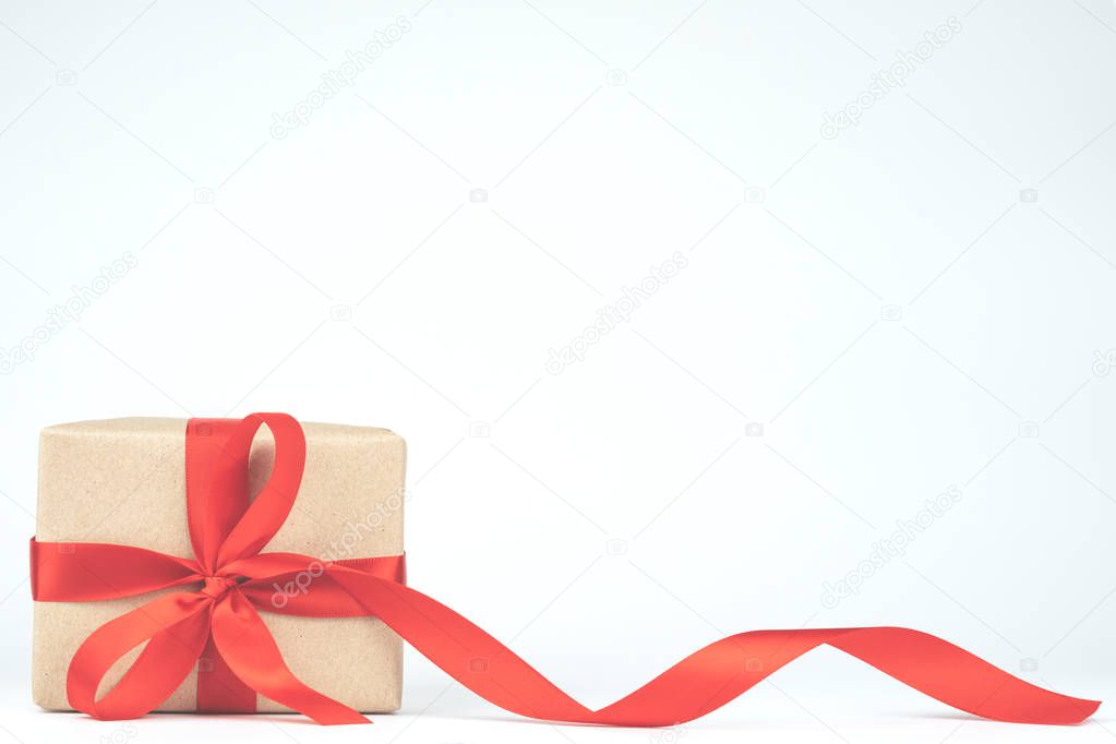 Wrapped handmade craft paper brown gift box with red ribbon bow isolated on white background. Christmas, New Year and happy birthday present decoration concept in vintage tone.