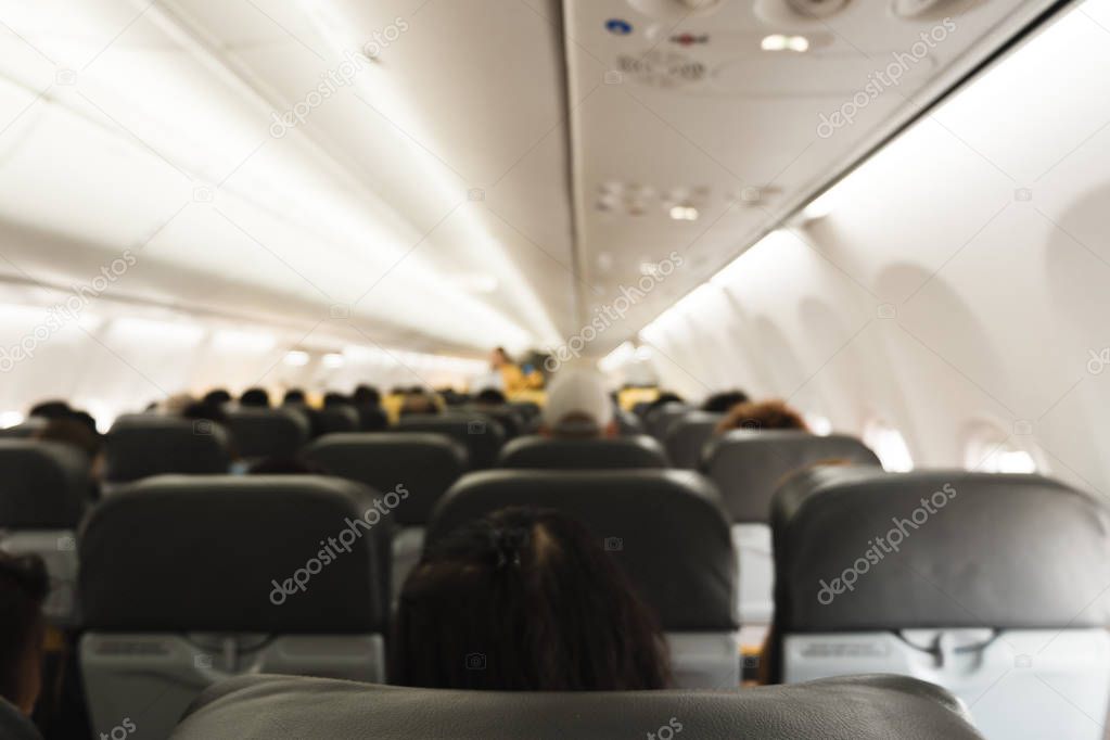 Blurred background of inside airplane. Rear view of passengers sitting on seats and stewardess walking to service customer in aisle. Interior of airplane.