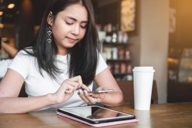  Dijital tablet pc ve kafede beyaz kahve fincanı ile tahta masada otururken Smartphone kullanan kadın