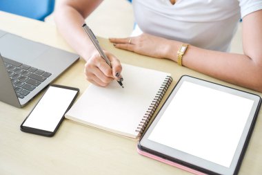 Asyalı kız öğrenci defter üzerinde dizüstü ve tablet pc, eğitim ve araştırma kavramı ile masada otururken yazma