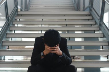 Genç Asyalı işadamı merdivenlerde oturan ve elleri ile kafa tutarak çalışma ve yaşam sorunları ile vurguladı