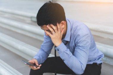 Genç Asyalı işadamı el smartphone ile beton merdivenlerde oturan iş ve yaşam sorunları ile vurguladı 