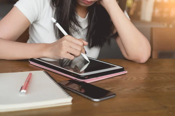 young asian freelancer woman holding touch pen in hand and working with digital tablet while sitting at table at cafe, Digital marketing concept