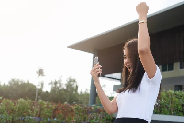 兴奋尖叫的年轻亚洲女子大学生阅读手机上的好消息 并举起手庆祝成功通过考试 得到了一份工作 快乐的女孩惊讶的表达实现一个目标 — 图库照片