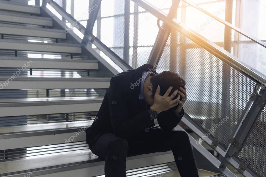 Young asian businessman stressed with work and life issues sitting on stairs and holding head with hands  