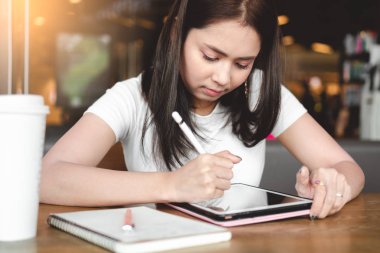 dokunmatik kalemi elinde tutan genç Asya serbest meslek sahibi kadın ve kahve Café, dijital pazarlama kavramı ile masada otururken dijital tablet ile çalışma 