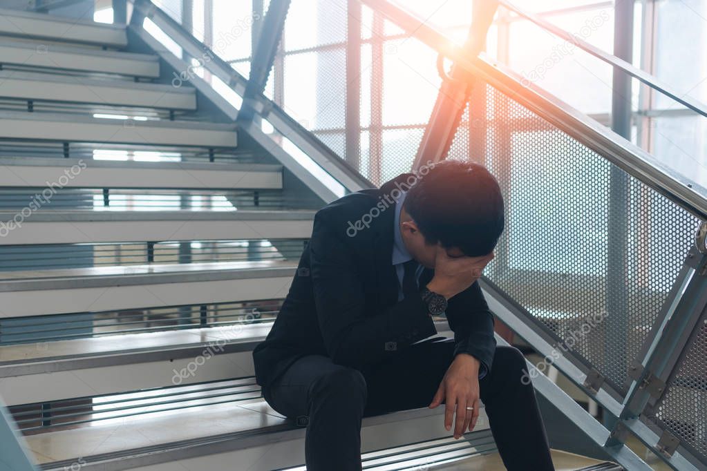 Young asian businessman stressed with work and life issues sitting on stairs and holding head with hand  