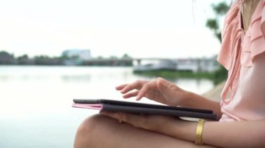 Genç Asyalı kadın el dijital tablet bilgisayar bilgi internet üzerinde arama kullanarak yakın açık akşam Nehri yakınında. El çalışma ve tablet ile yazarak.