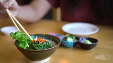 Ağır çekim genç kadın el wakame deniz yosunu salata Japon lokantasında yemek yemek çubukları ile. Geleneksel Japon lezzetli taze deniz yosunu salata kasesine.