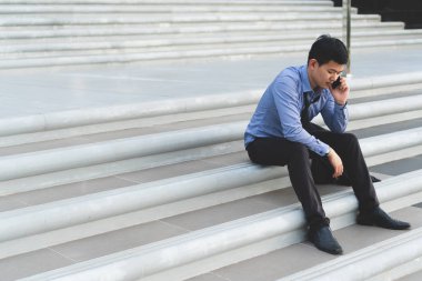 Beton merdiven telefonda konuşurken oturan genç Asyalı işadamı ne zaman vurgulayarak biliyorum iş başarısız olduğunu ve işsiz. Aileden kötü haber aldıktan sonra duygusal depresif.