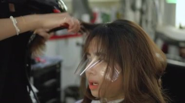 Bir saç kurutma makinesi kurutma kullanarak ve saç kıvırma profesyonel kuaför. Genç Asyalı kadın onun Kuaför Saç salonda alma. Saç kurutma makinesi kullanarak kadın stilist kadar kapatın. Güzellik Salonu.