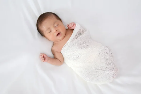 Спящий новорожденный ребенок в белой обертке во время на белом одеяле назад — стоковое фото