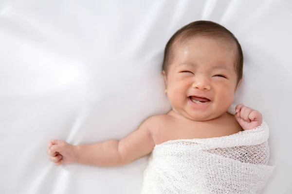 Sorrindo bebê recém-nascido adorável em envoltório branco enquanto deitado no branco — Fotografia de Stock